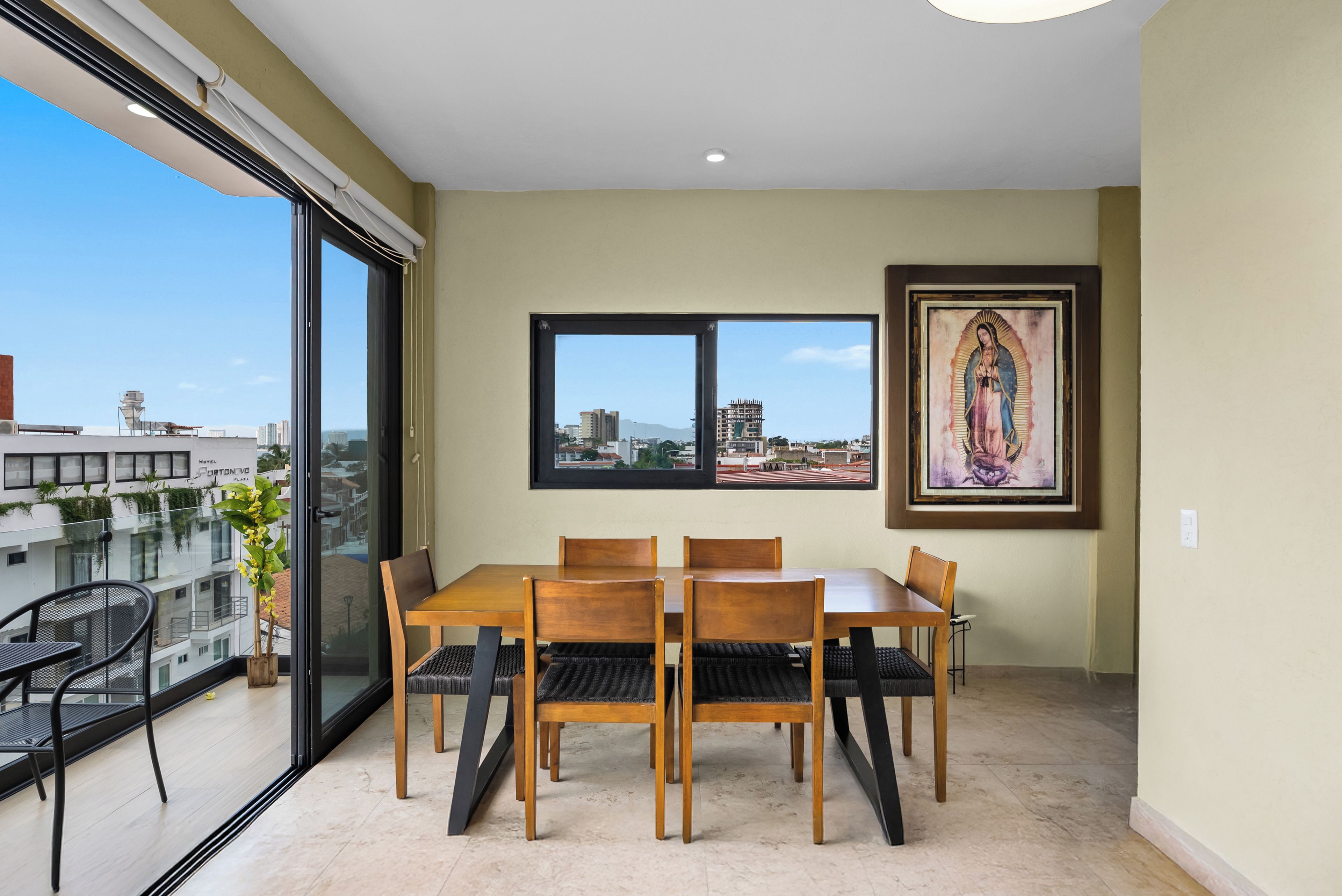 Ein Essbereich mit Tisch und Stühlen, ein großes Fenster mit Stadtblick und ein gerahmtes Kunstwerk an der Wand.
