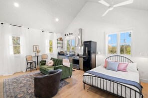 Quarto moderno com cama, escrivaninha e um pequeno espaço de cozinha.