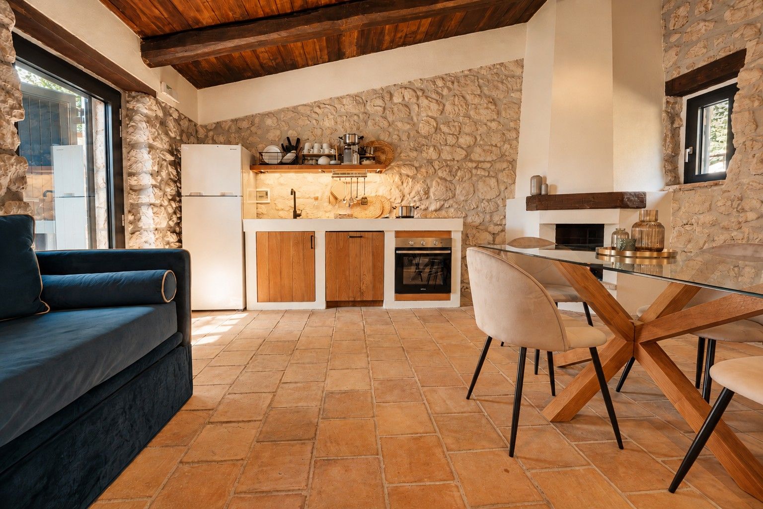 A modern kitchen with stone walls, a built-in oven, and a dining area with a glass table and chairs.