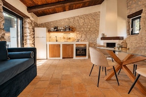 Una cocina moderna con paredes de piedra, horno empotrado y zona de comedor con mesa y sillas de vidrio.