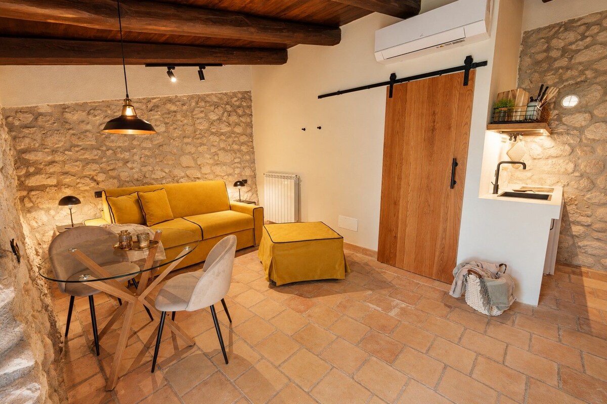 A cozy living area with a sofa, a glass table, and chairs, a wooden door, and a stone wall.