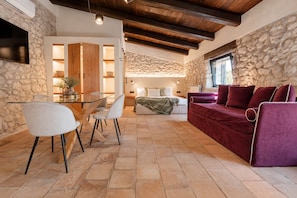 A cozy living area with a stone wall, a wooden ceiling, a purple sofa, and a dining table with chairs.