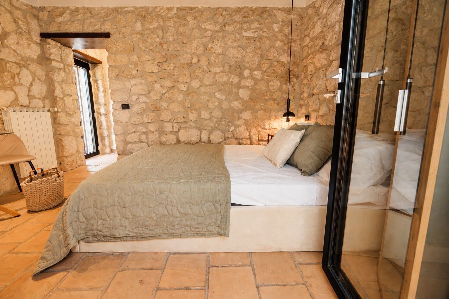 A bedroom with a stone wall, a bed with white bedding, a hanging light fixture, and a wooden floor.