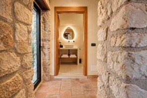 A stone-walled bathroom with a wooden door, a round mirror, and a sink.