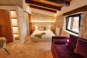 A bedroom with a bed, a wooden wardrobe, a stone wall, a window, and a red sofa.