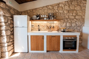A compact kitchen with a stone wall, a white refrigerator, wooden cabinets, and a built-in oven.