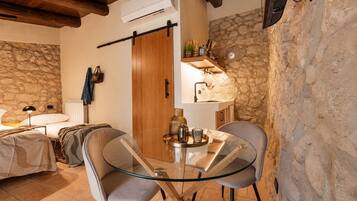 Una stanza accogliente con parete in pietra, porta in legno, un letto, un tavolo con sedie e una pianta pensile.