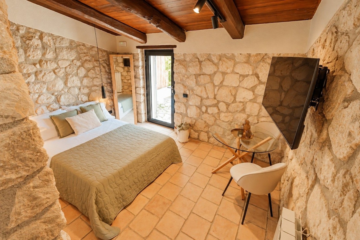 A bedroom with a stone wall, a bed with a quilt, a chair, and a TV mounted on the wall.