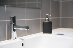 A modern bathroom with a chrome faucet, a white sink, and a black soap dispenser. - GuestReady - PoetikBlue - Studio 1 (Porto)