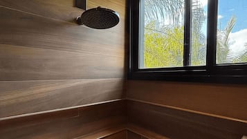 Canto de um quarto com painéis de madeira, uma janela com vista para árvores e céu, e um luminário fixado na parede.
