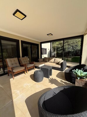 A sunlit outdoor seating area with a sofa, chairs, and a wicker table. - Chácara Rockie offers an experience of comfort, elegance, and exclusivity. (Itatiba)
