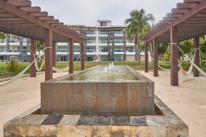 A rectangular water feature with a fountain in the center, surrounded by a wooden pergola structure. - Mareazul luxury condo | Beach & Resort Pools (Playa del Carmen)