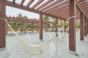 Eine Hängematte unter einer Holzpergola, im Hintergrund ein Wasserspiel.