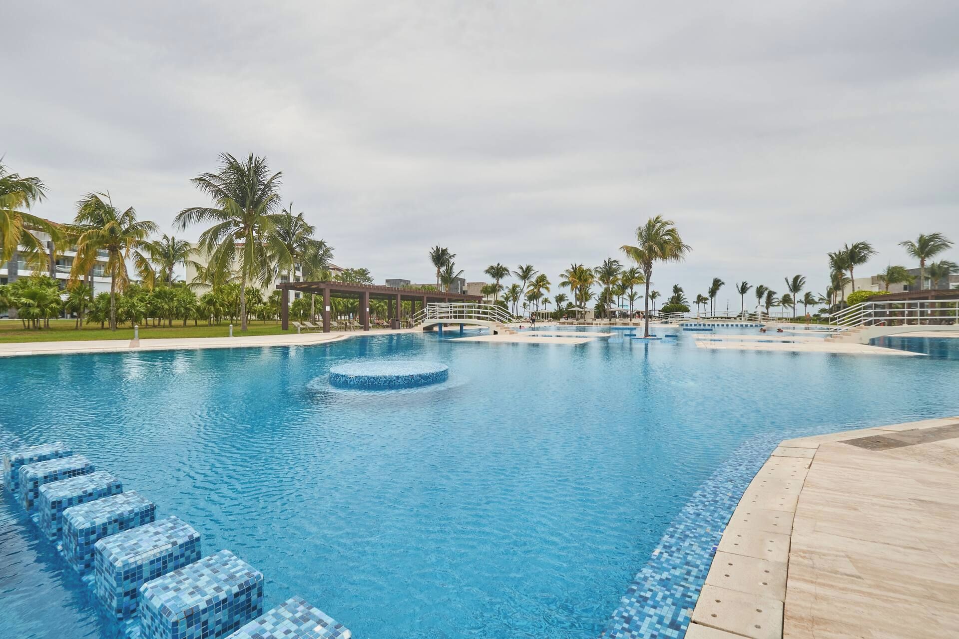 A large outdoor swimming pool with multiple lanes, surrounded by palm trees and a covered walkway.