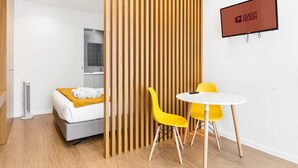 A hotel room with a bed, a wooden partition, a TV screen, and a table with chairs. - GuestReady - PoetikBlue - Studio 4 (Porto)