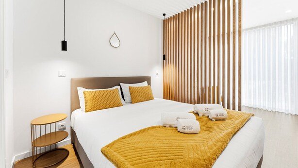 A modern hotel room with a large bed, a wooden headboard, a round side table, and a decorative wall panel. - GuestReady - PoetikBlue - Studio 4 (Porto)