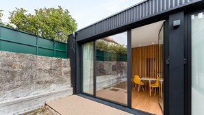 A modern building with a glass door leading to an interior space with a dining table and chairs. - GuestReady - PoetikBlue - Studio 4 (Porto)