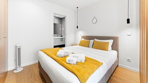 A hotel room with a bed, a bedside table, a mirror, a wall-mounted light, and a thermostat. - GuestReady - PoetikBlue - Studio 4 (Porto)