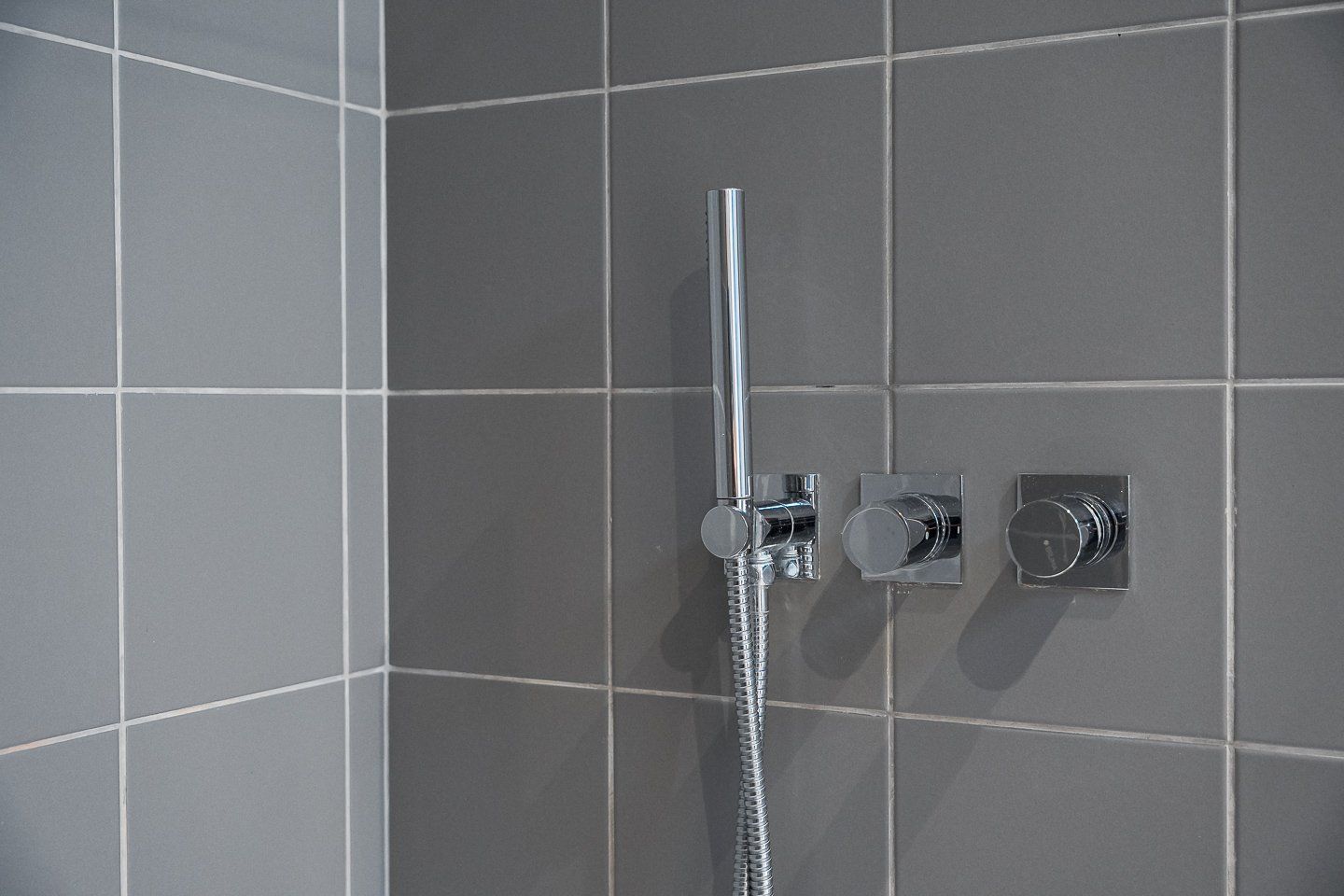 A shower with a chrome faucet and hose, mounted on a tiled wall.