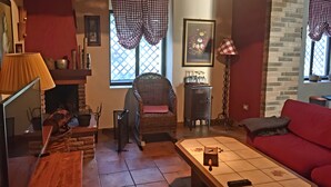 A cozy living room with a fireplace, a red sofa, a wicker chair, and a tiled coffee table.