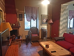 Ein gemütliches Wohnzimmer mit Kamin, einem roten Sofa, einem Korbstuhl und einem gefliesten Couchtisch.