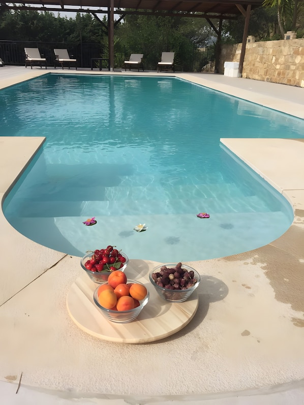 A swimming pool with lounge chairs and a fruit bowl on the deck.