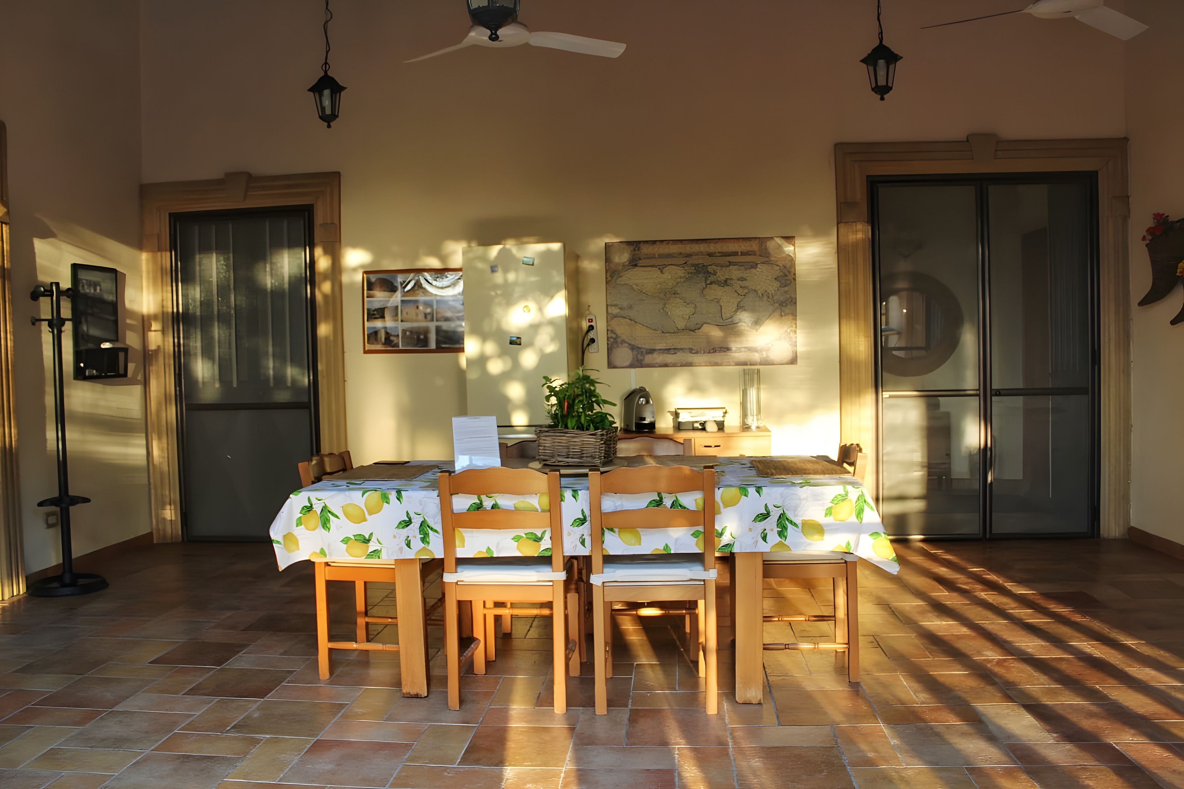 A dining area with a table set for four, wooden chairs, a ceiling fan, and a world map on the wall.