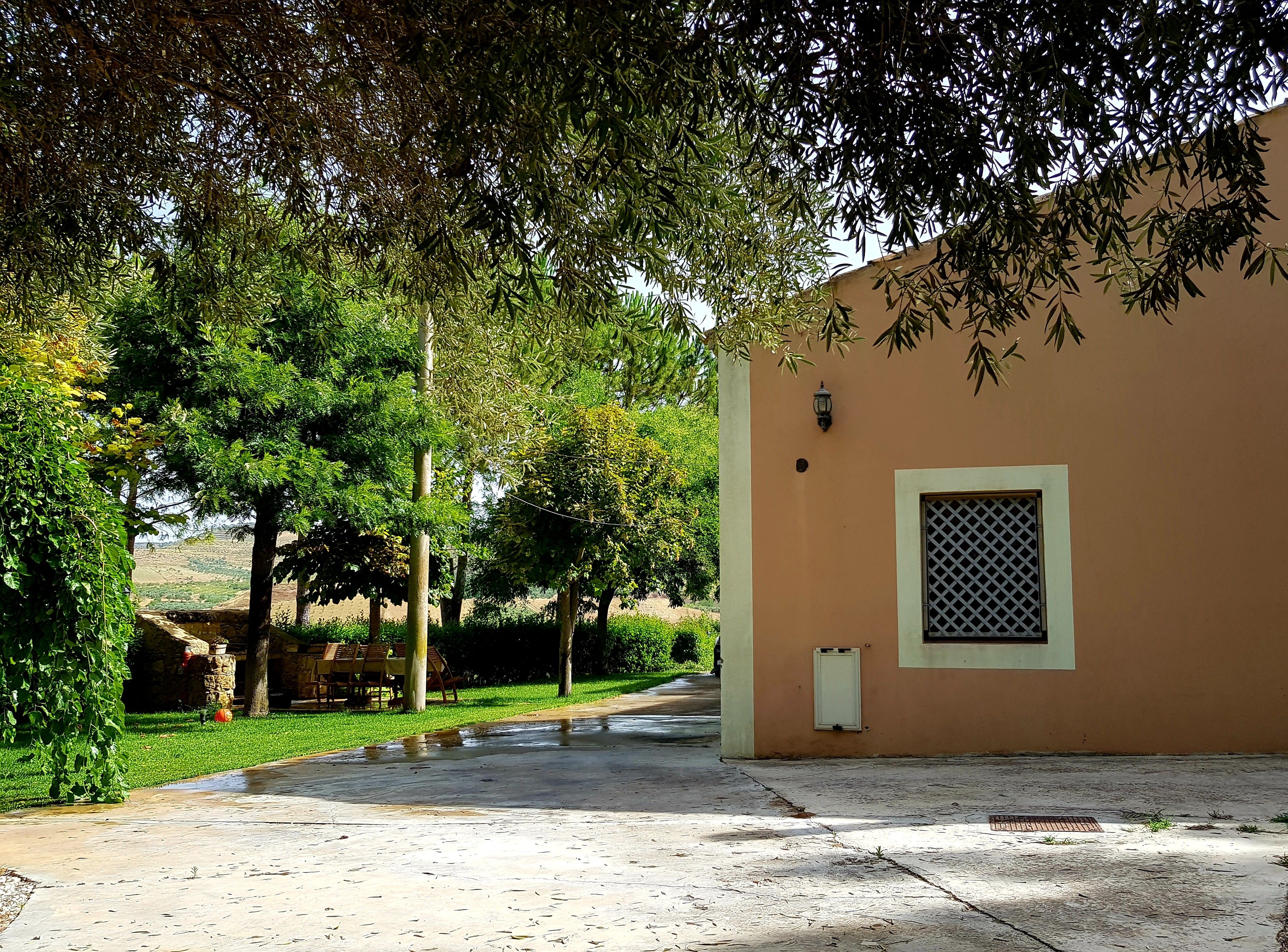 A building with a paved entrance, a small window with a lattice design, and a wall-mounted light fixture.