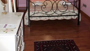 Ein Schlafzimmer mit Holzboden, einem Bett mit floralem Bettzeug, einem Nachttisch mit Lampe und einem Spiegel.