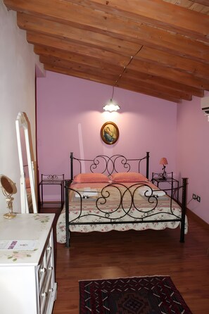 Una camera da letto con soffitto in legno, un letto con lenzuola a motivi floreali, un comodino con una lampada e uno specchio.