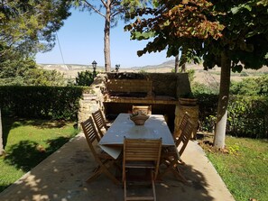 Zona pranzo all'aperto con barbecue in pietra e tavolo apparecchiato per quattro persone.
