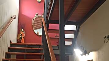 A staircase with wooden steps and a black handrail, leading to a red wall with a decorative mirror and a framed picture.