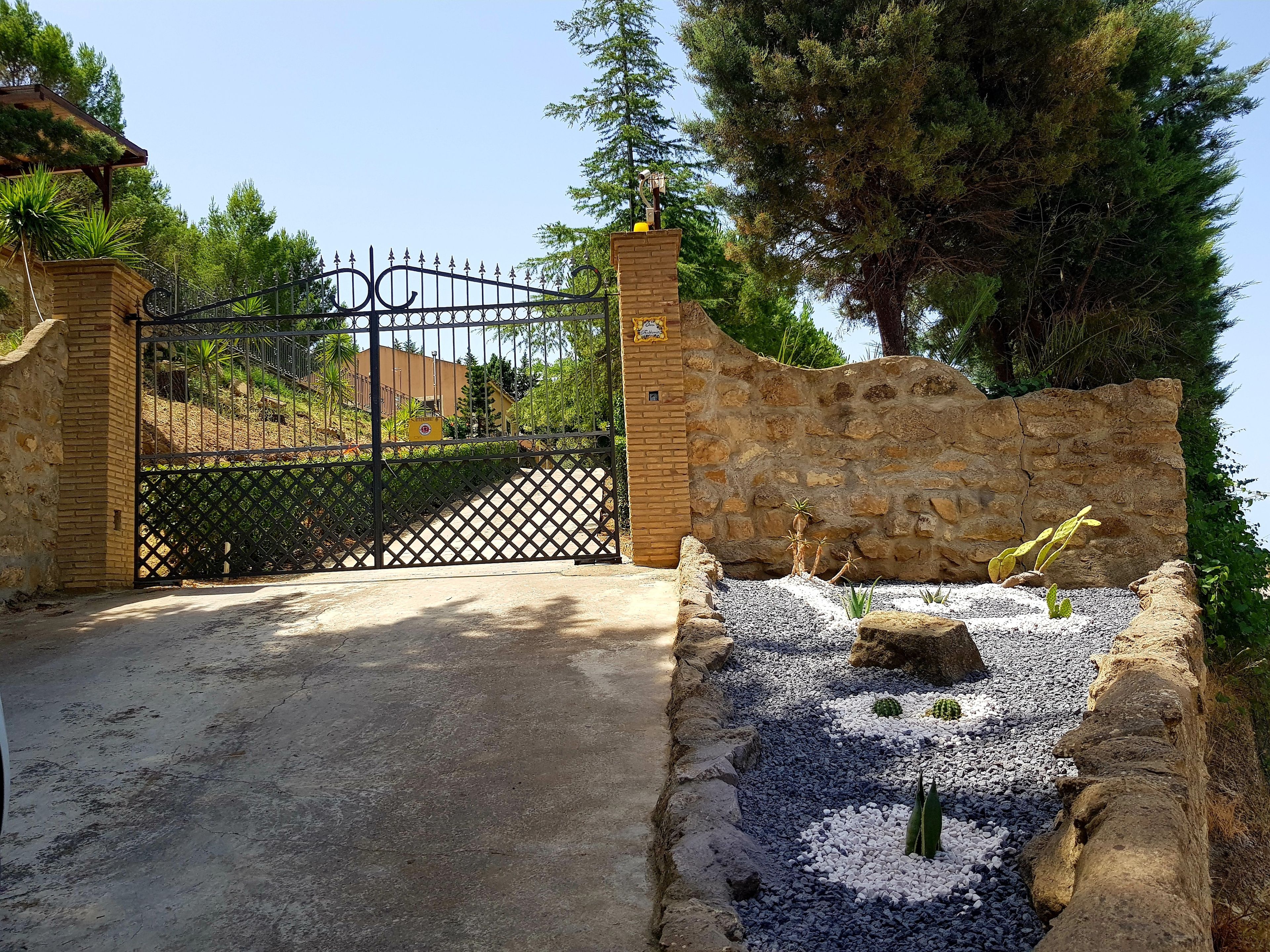 Una entrada protegida por un portón metálico, un muro de piedra y un camino de grava que lleva a un edificio.