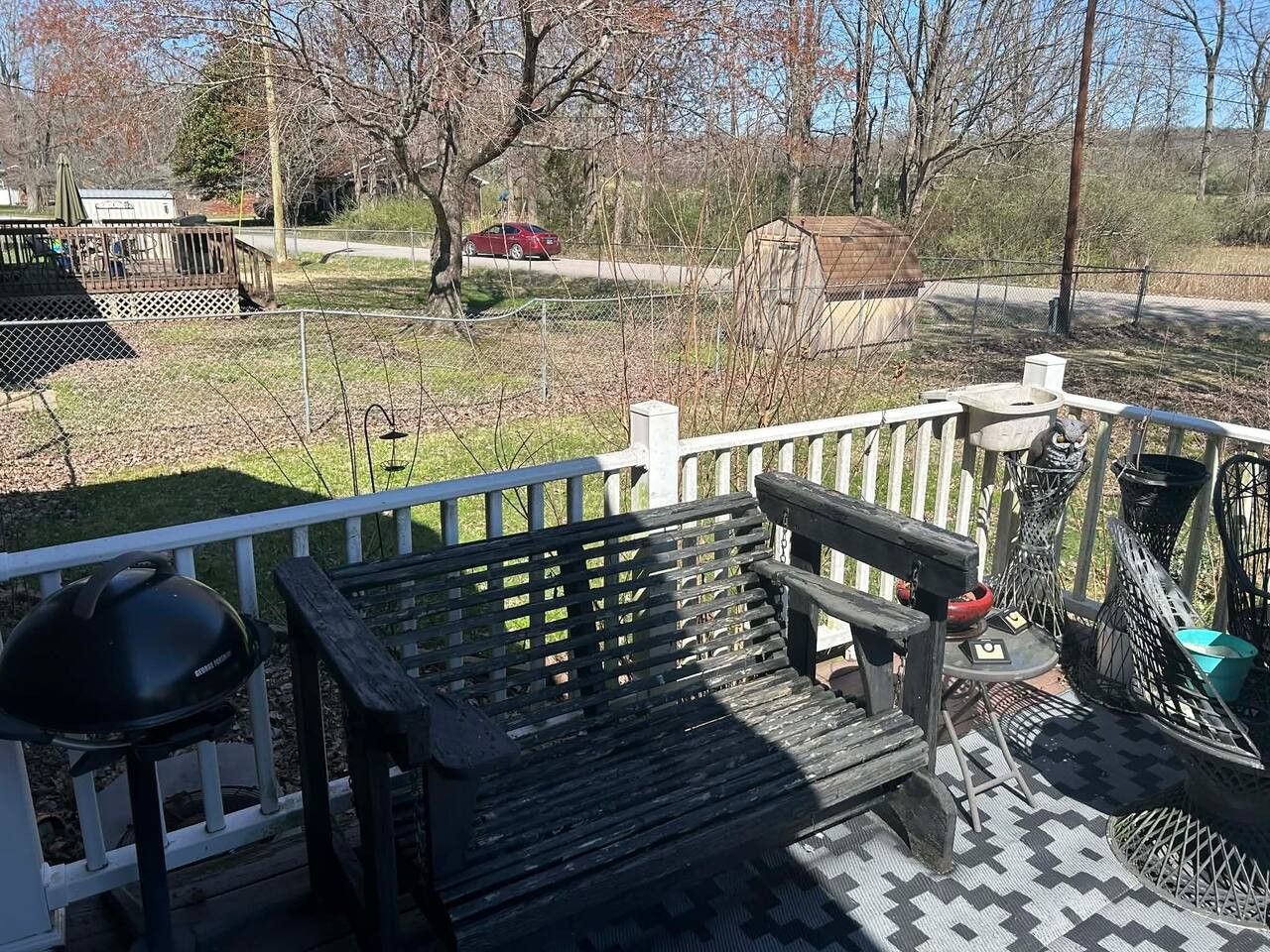 A patio area with a wooden bench, a grill, and a fenced garden.