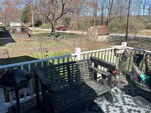 A patio area with a wooden bench, a grill, and a fenced garden.