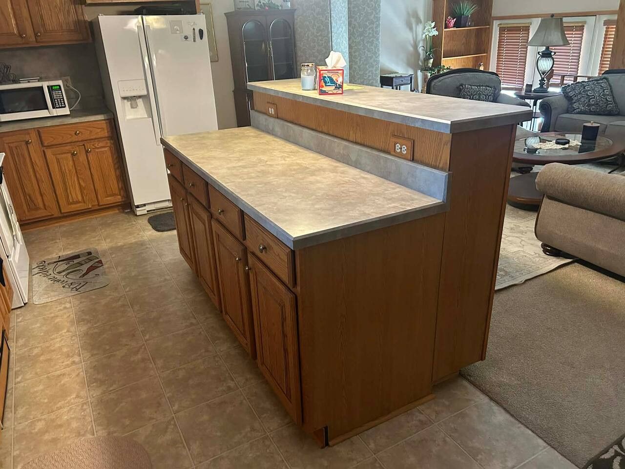 A kitchen with wooden cabinets, a built-in island, a refrigerator, and a microwave.
