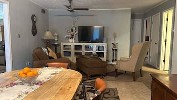 A living room with a dining table, sofas, a television, and a ceiling fan.