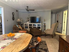 Una sala de estar con una mesa de comedor, sofás, un televisor y un ventilador de techo.