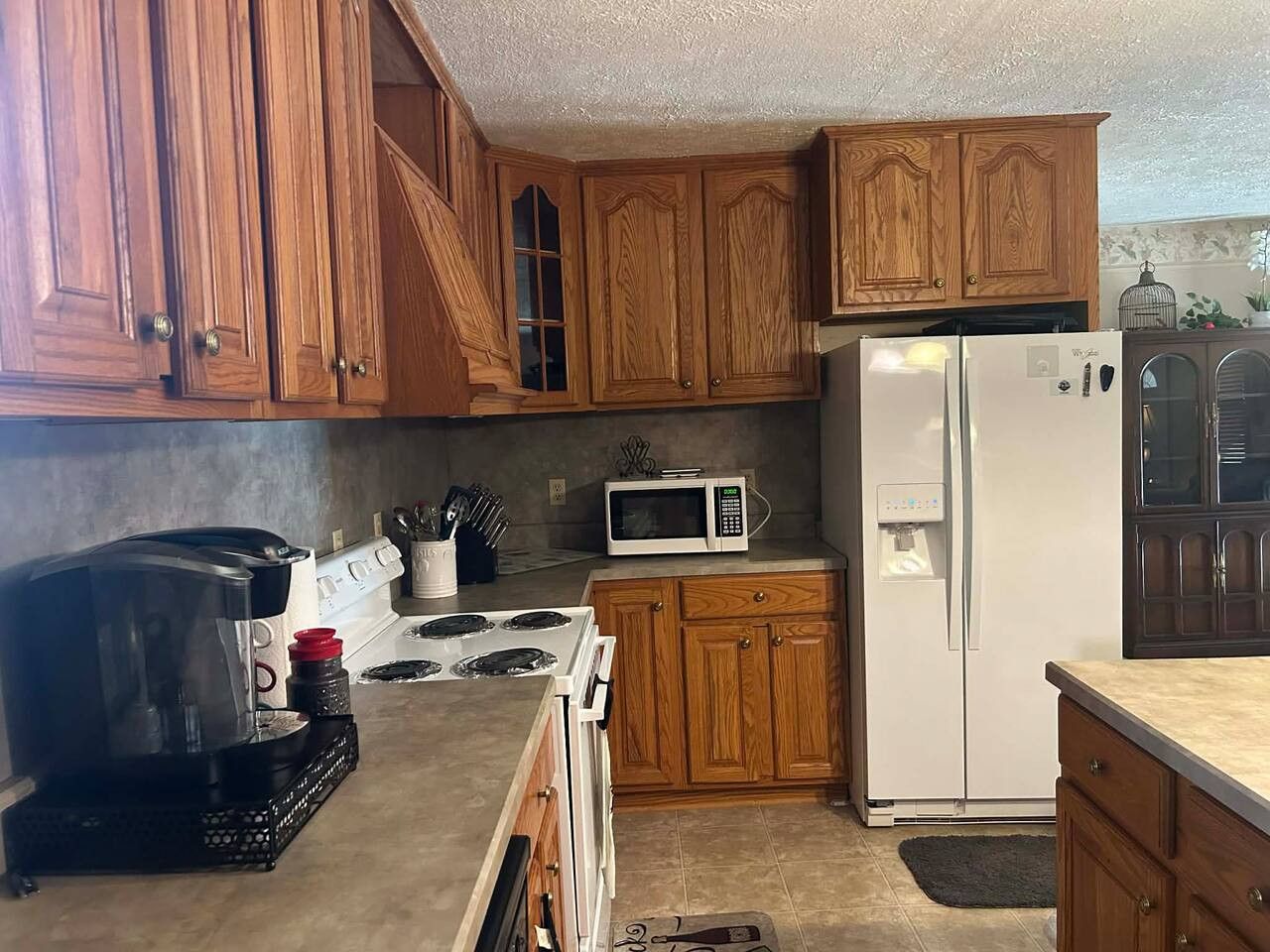 A kitchen with wooden cabinets, a white refrigerator, a microwave, a stove, and a coffee maker.