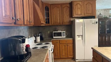 A kitchen with wooden cabinets, a white refrigerator, a microwave, a stove, and a coffee maker.
