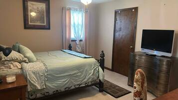 A bedroom with a bed, a television on a stand, a ceiling fan, a door, and a window with curtains.