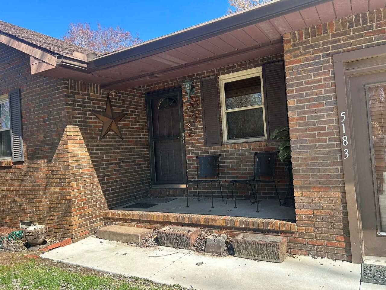 A brick house with a front porch, a star decoration, and a number '5183' on the door.