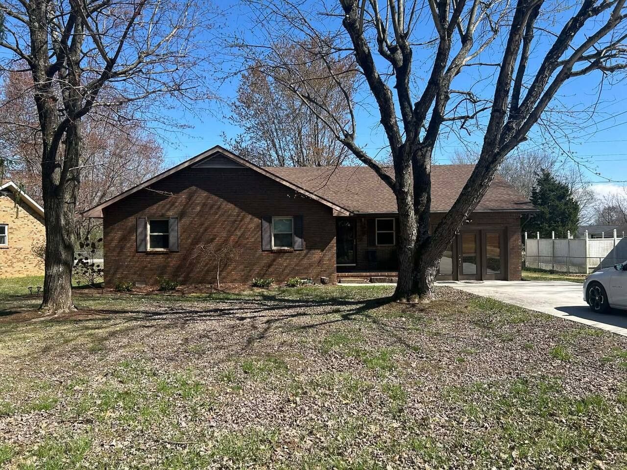 A single-story brick house with a sloped roof, a front porch, and a driveway.