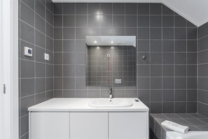 A modern bathroom with a white sink, dark tiles, a mirror, and a towel on the counter. - GuestReady - PoetikBlue - Room 4 (Porto)