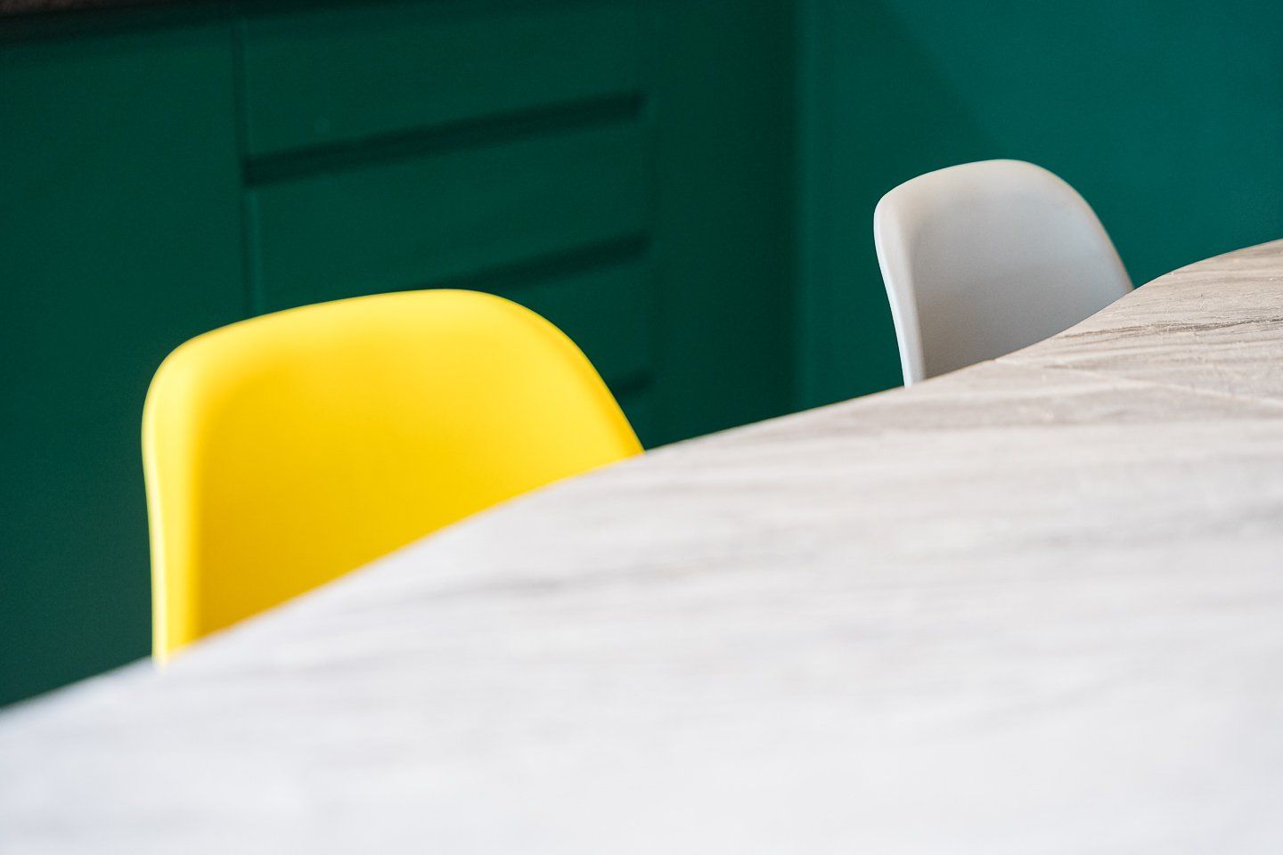 Mesa com superfície branca e duas cadeiras, uma amarela e outra branca, em um quarto com paredes verdes.