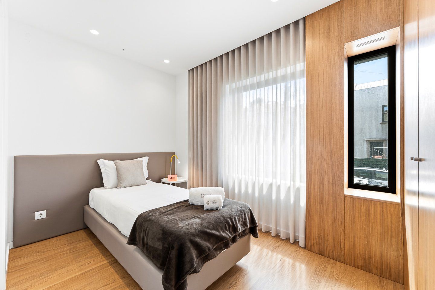 Ein modernes Hotelzimmer mit einem großen Bett, einem Nachttisch, einer Lampe und einem Fenster mit Vorhängen.