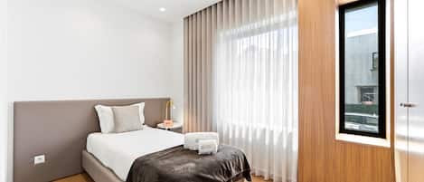 Ein modernes Hotelzimmer mit einem großen Bett, einem Nachttisch, einer Lampe und einem Fenster mit Vorhängen.