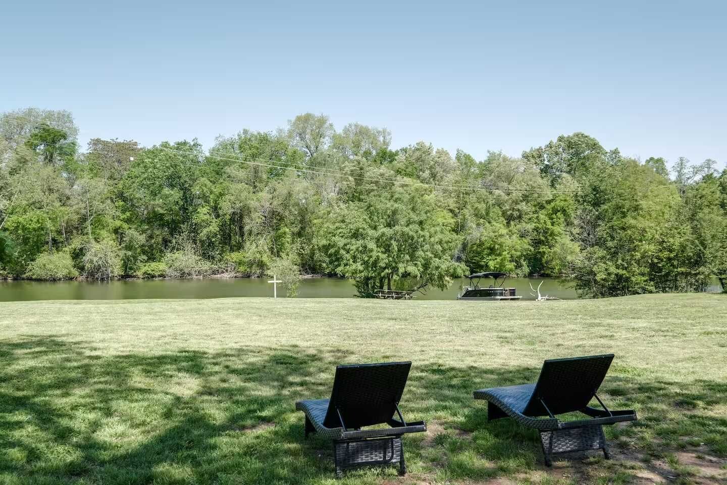 A grassy area with two wicker chairs facing a body of water, surrounded by trees.