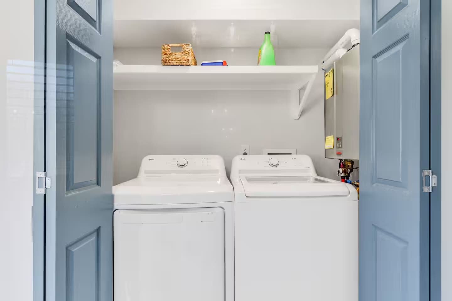 A laundry room with two white washing machines, a wicker basket, and a green bottle on a shelf.