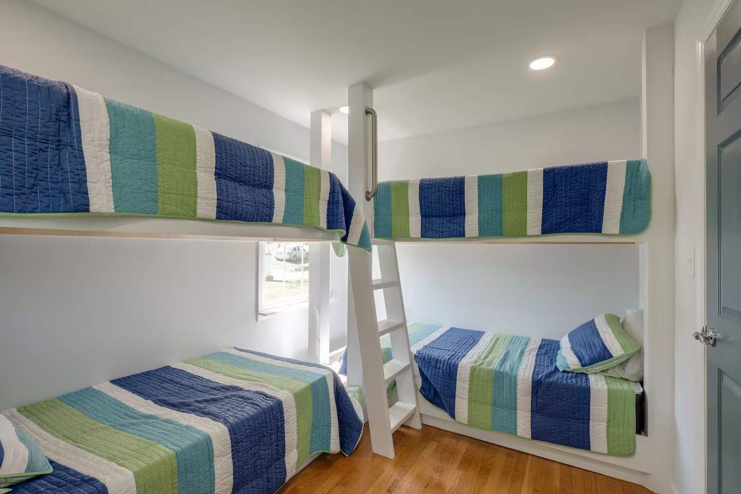 A bunk bed room with a ladder, white walls, and a window.